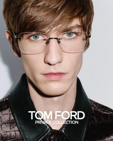 Close-up of a fair-skinned adult male model with light brown hair and blue eyes wearing rimless eyeglasses against a white background.
