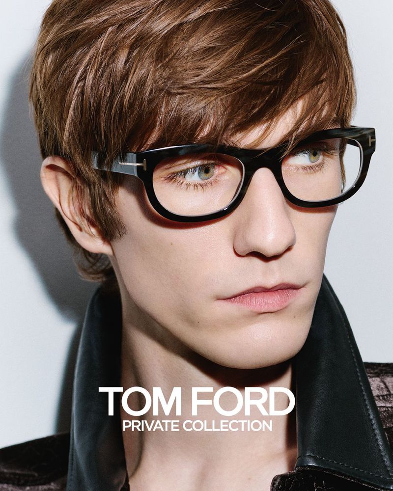 Close-up portrait of a fair-skinned adult male wearing black-rimmed glasses and a leather jacket, with 'TOM FORD' text visible.