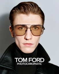 Close-up portrait of a male model wearing tinted aviator sunglasses and a black leather jacket against a grey backdrop.