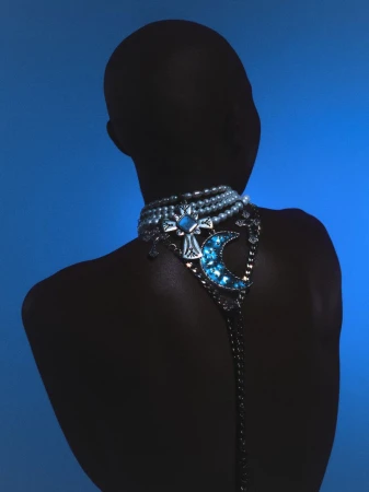 Back view of a person with bare skin, wearing an elaborate pearl and gemstone necklace against a gradient blue background.