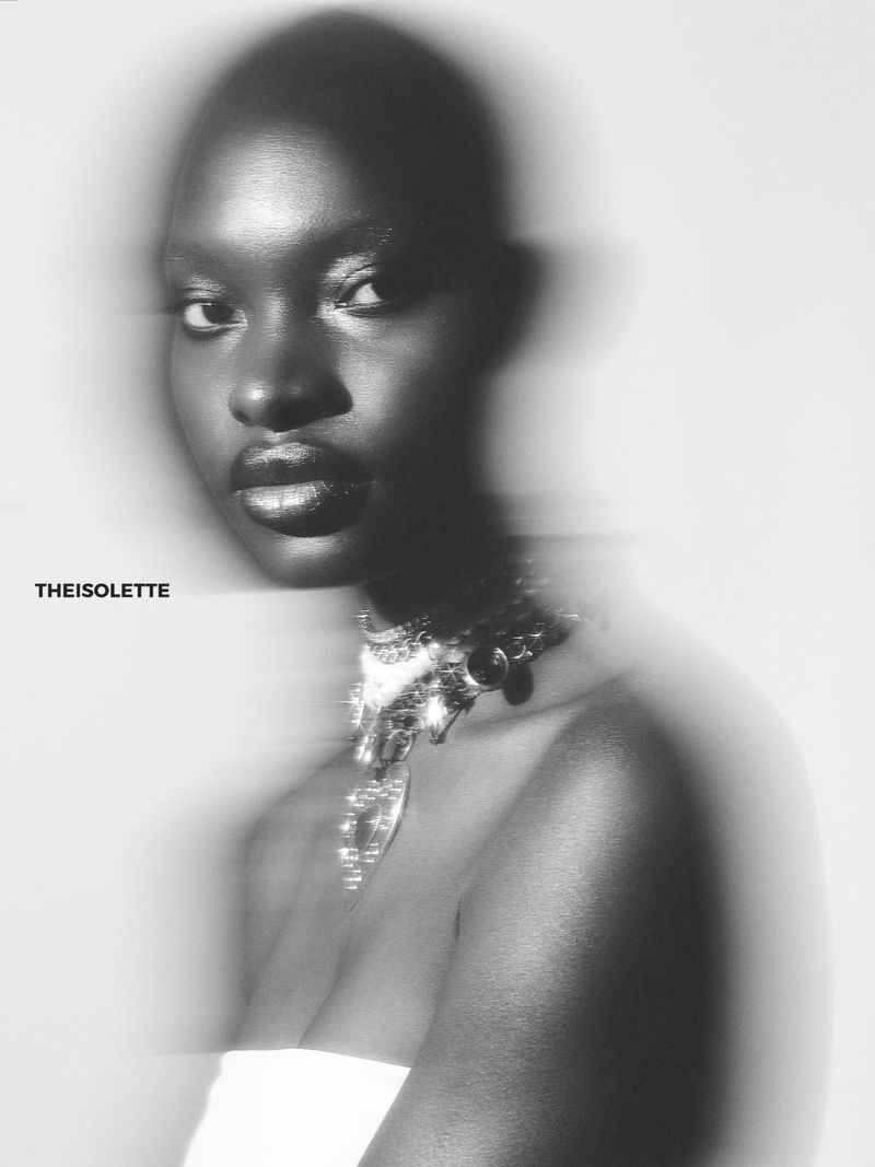 Monochromatic portrait of a Black adult female model wearing jewelry with soft-focus effect and studio lighting on a light backdrop.
