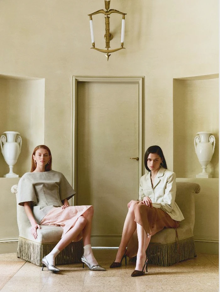 Two female models seated in armchairs against a pale wall with decorative urns for Jonak Fall Winter 2024 lookbook.