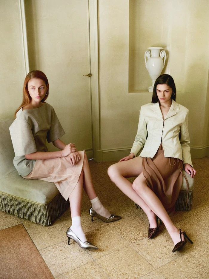 Two female models seated in an interior room wearing stylish neutral clothing and heeled shoes for Jonak Fall Winter 2024 lookbook
