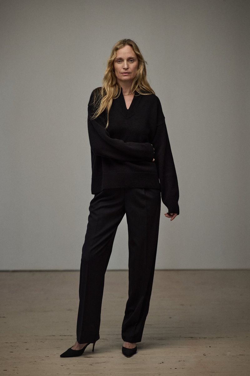 Model Amy Wesson wearing a black V-neck sweater and black trousers in a studio setting.