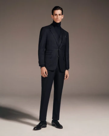 Studio shot of an adult male model wearing a navy blue three-piece suit with a turtleneck sweater and leather dress shoes.