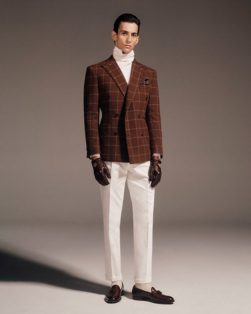 Full-length shot of adult male in brown plaid suit, white turtleneck, and brown leather gloves and loafers posing in a studio.