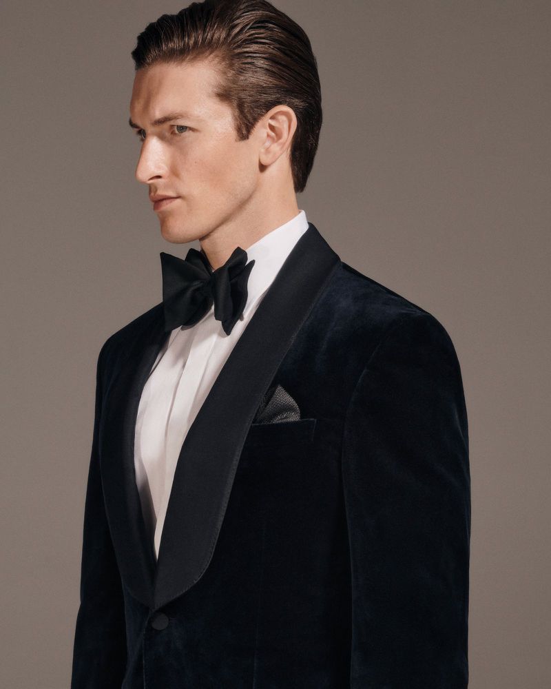 Elegant man in a black velvet tuxedo with a bow tie and pocket square, captured in a studio setting with soft lighting.