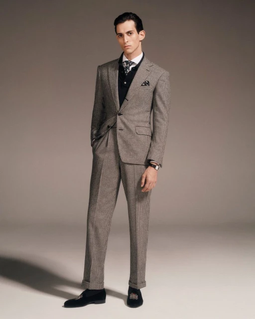 Portrait of a young adult male in a checkered suit, wearing a vest and tie, posing indoors in a fashion or editorial style photograph.