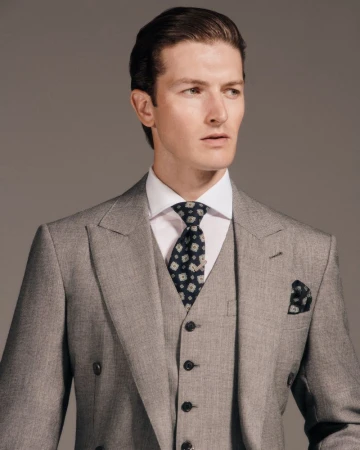 Man wearing a grey three-piece suit with a patterned tie and pocket square against a neutral studio backdrop