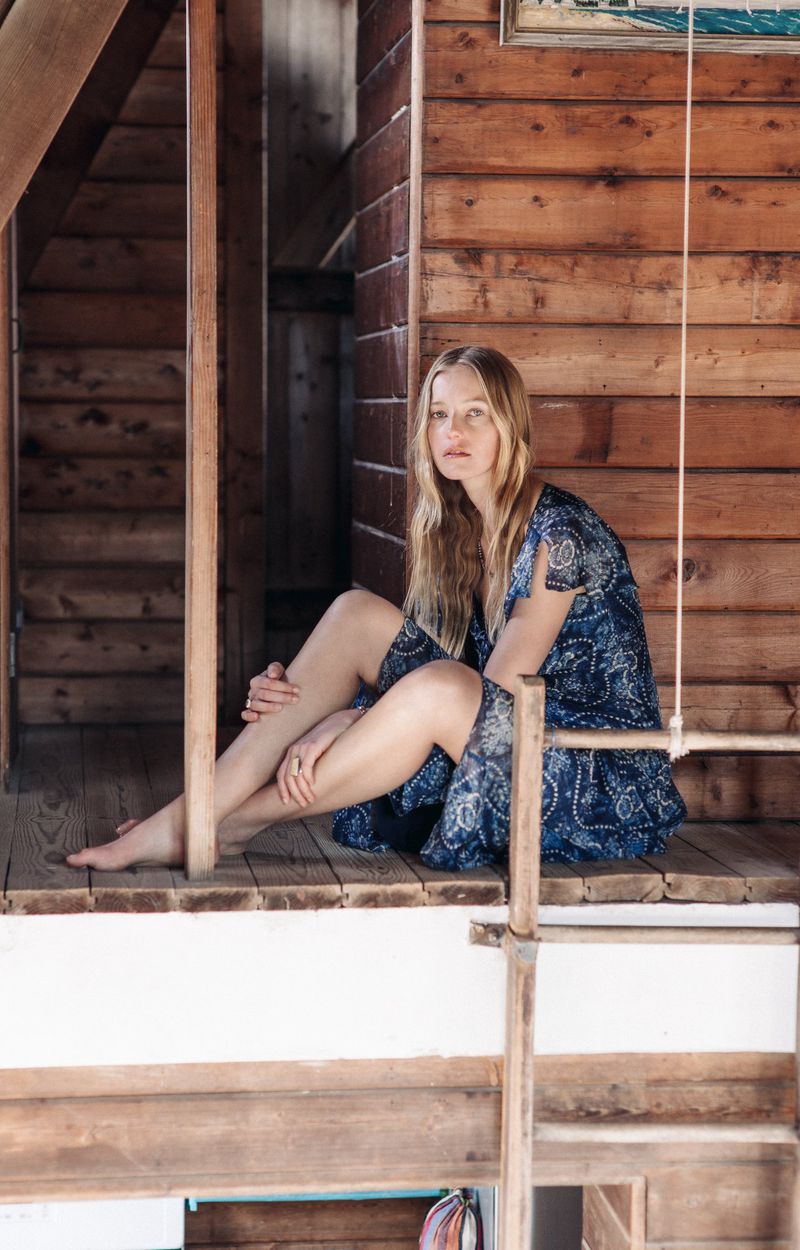 Model Natalie Ludwig sitting on a wooden porch wearing a blue patterned dress for the Ralph Lauren Double RL campaign.