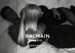 Monochrome shot of a man and blonde woman reclining on white bedsheets for Balmain Hair Couture.