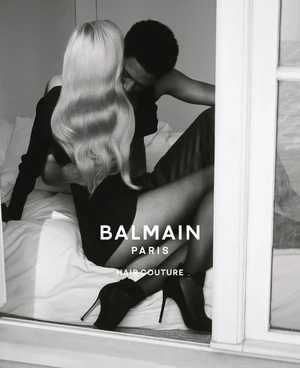 Black and white editorial image of a blonde woman and a man embracing on a bed for Balmain Hair