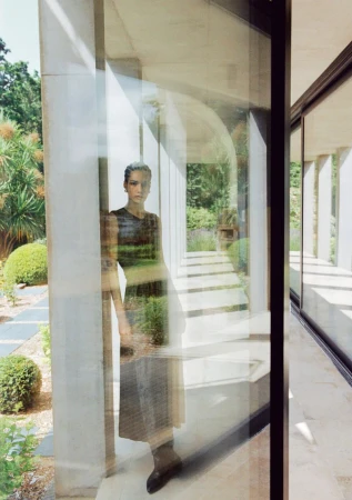 Adult woman in dress reflected in a modern building's glass exterior, showcasing architectural design with natural light and landscape.