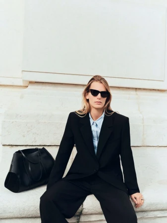 Woman with sunglasses in blazer sitting on stairs with tote bag. Stylish fashion and outdoor setting for lifestyle photoshoot.
