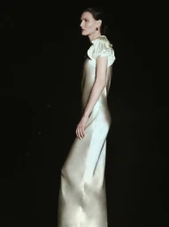 Model in profile wearing a cream silk dress with puffed sleeves against a dark background for Altuzarra