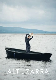 Model wearing a dark polka dot dress standing inside a dark rowboat floating on an open lake under an overcast sky
