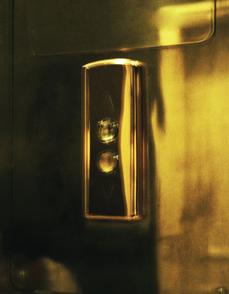 Close-up of a golden elevator button panel with up and down directional arrows on a metal surface, casting soft shadows.