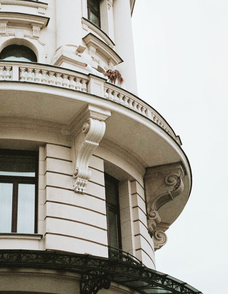 Elegant architectural detail of a curved white building with wrought iron accents, showcasing ornate exterior and window placement under an overcast sky.