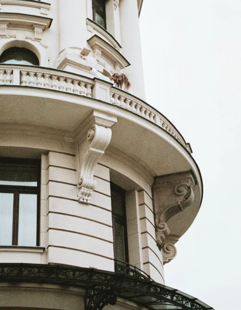 Elegant architectural detail of a curved white building with wrought iron accents, showcasing ornate exterior and window placement under an overcast sky.