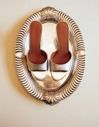 Pair of silver metallic high-heel sandals resting on an ornate vintage silver platter against a plain background