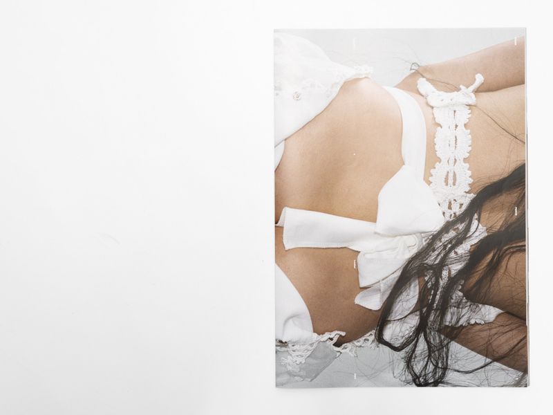 Woman lying down wearing white lingerie in photo studio with diffused lighting, lace details, and long dark hair.