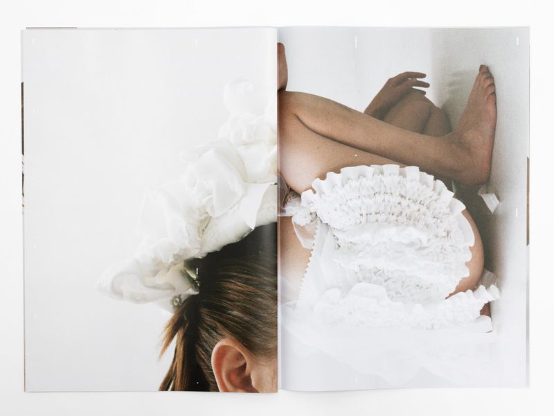 Cropped shot of a partially visible woman wearing ruffled white fabric, laying in a white cardboard box. Magazine spread style image.