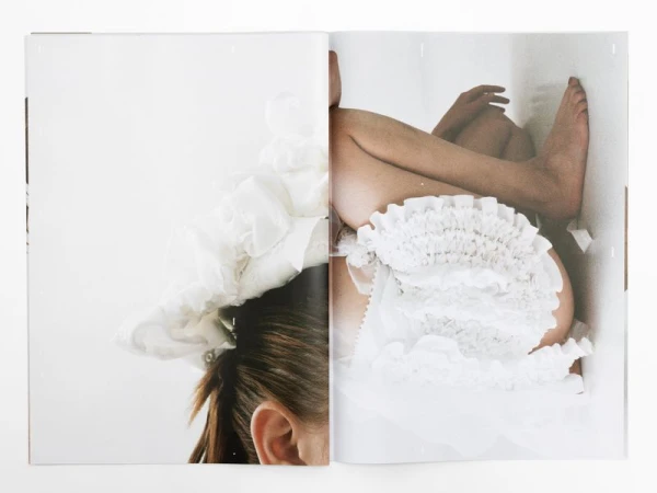 Cropped shot of a partially visible woman wearing ruffled white fabric, laying in a white cardboard box. Magazine spread style image.