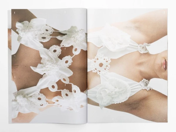 Editorial shot of two partial figures, featuring fair skin and wearing white floral accented attire against a bright white backdrop.