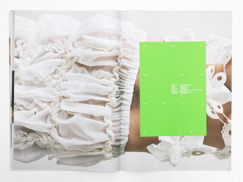 Open magazine spread featuring a model in a ruffled white dress, overlaid with a bright green block with text, against a white backdrop.