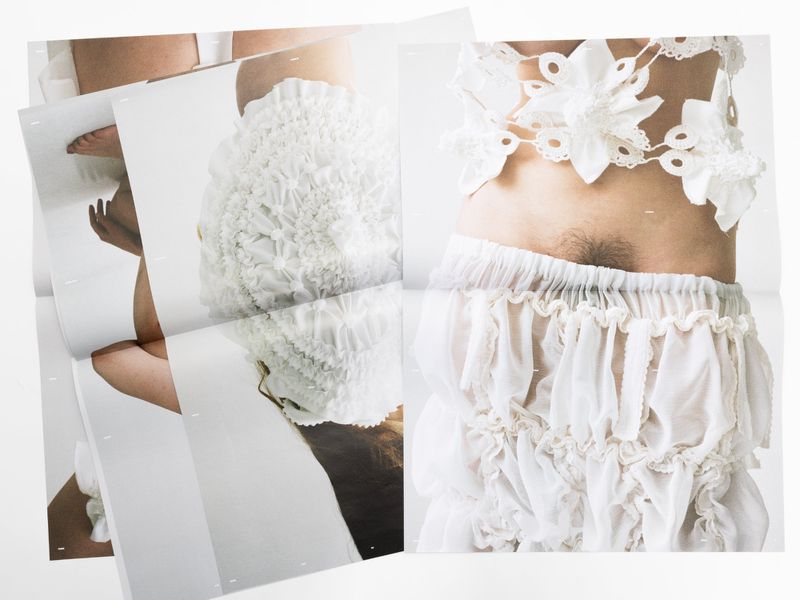 Conceptual fashion photograph featuring a person wearing decorative, handmade white textile garments in a minimalist setting on a white background.