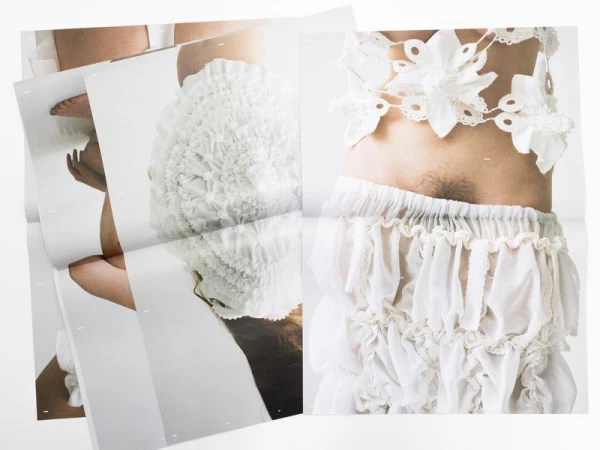 Conceptual fashion photograph featuring a person wearing decorative, handmade white textile garments in a minimalist setting on a white background.