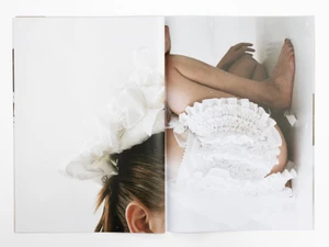 Model curled up in white ruffled garments against a light background in a spread layout for Roisin Pierce