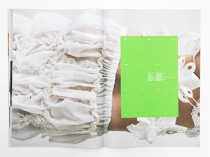 Close-up of an open publication spread showing textured white ruffled fabric and crochet details with a bright green text box.