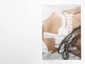 Close-up of a person wearing white lace garments with long dark hair against a plain background
