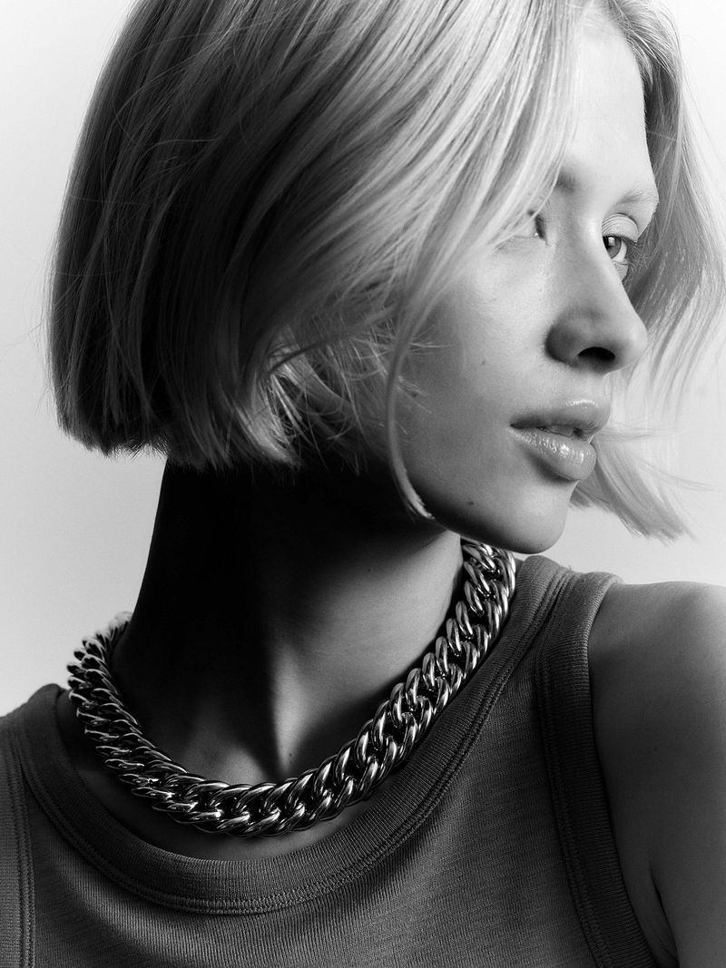Close-up black-and-white portrait of a young woman with blond hair and a tank top, wearing a large metal chain necklace.