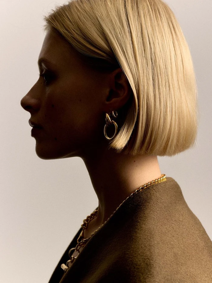 Profile portrait of a blonde woman wearing gold hoop earrings and a gold chain necklace for Tilly Sveaas