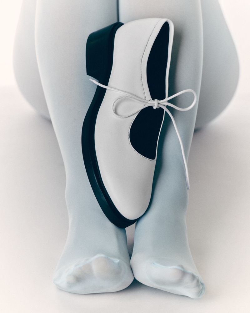 White and black dress shoe displayed against the legs of a figure wearing light blue tights, creating a minimalist fashion statement.