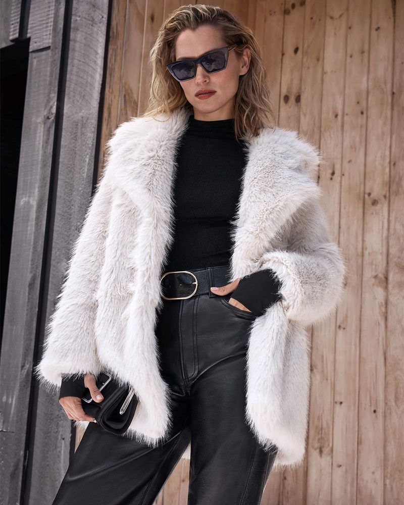 A woman poses in a furry coat and black leather pants against a wooden background, showcasing a blend of textures and fashion styles.