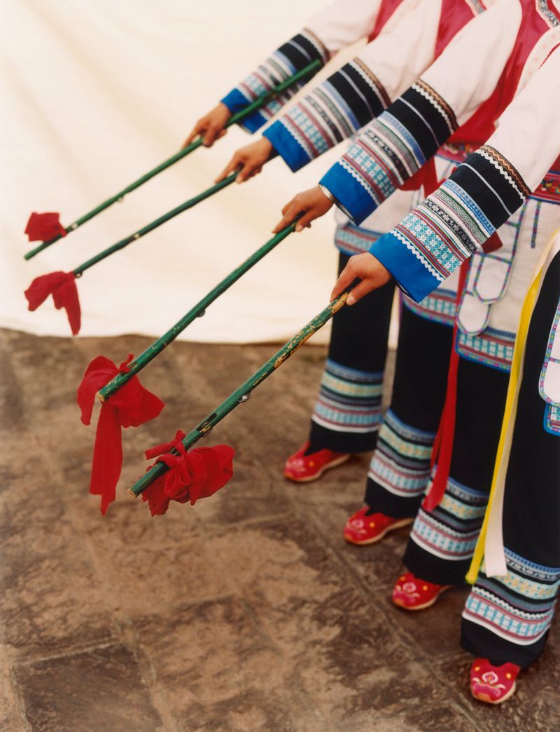 Unidentifiable ethnicity group of people performing a traditional dance with red tassel sticks, wearing colorful ethnic clothing in a studio.