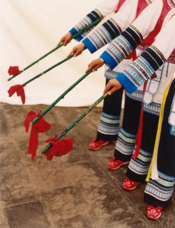 Unidentifiable ethnicity group of people performing a traditional dance with red tassel sticks, wearing colorful ethnic clothing in a studio.