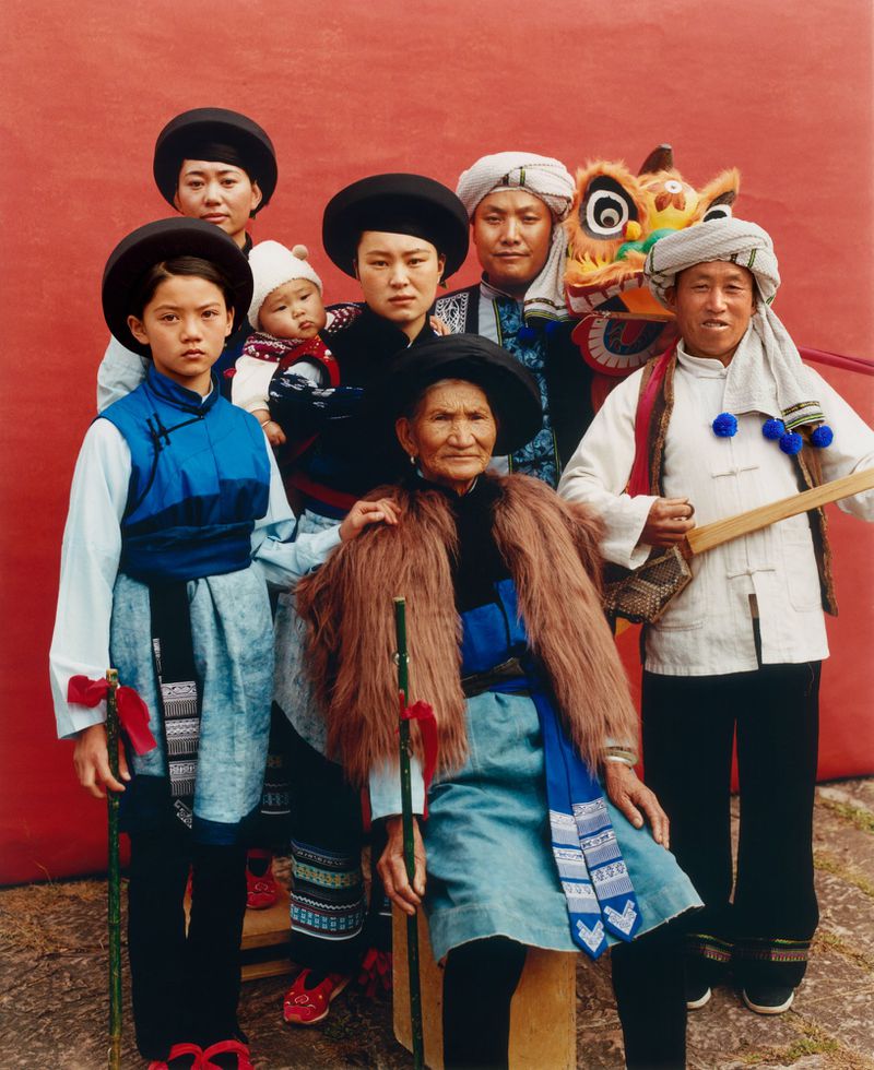 Group portrait of a multigenerational Chinese family in traditional clothing against a solid red background. Focus on their cultural attire.