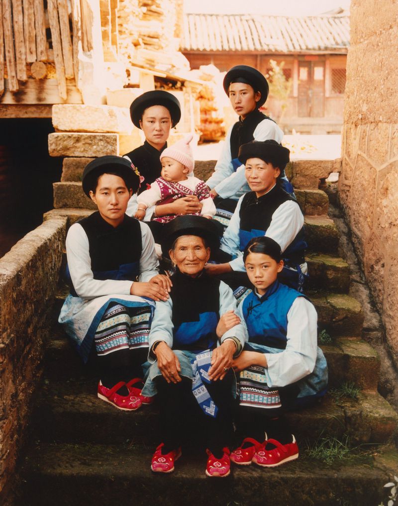 Group portrait of seven people, including a baby, seated on stone steps wearing traditional clothing outdoors during the daytime.
