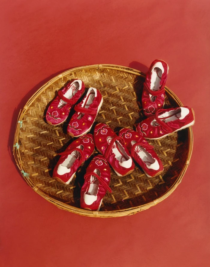 Several red embroidered shoes arranged inside a large round woven bamboo tray on a red surface