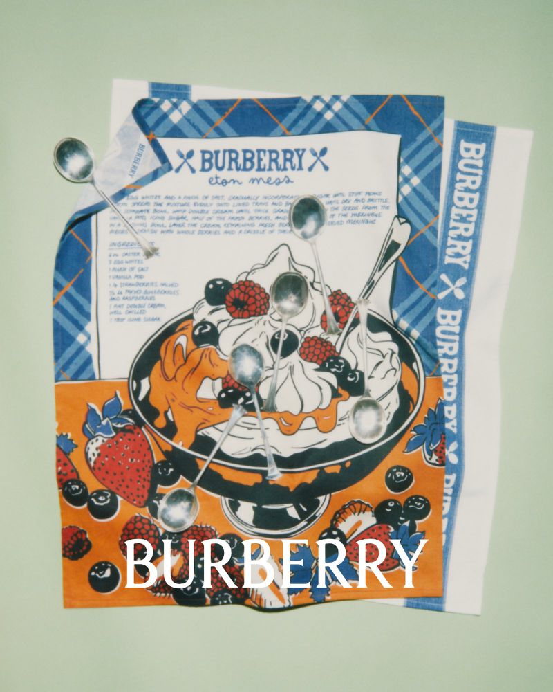 Stylized product shot of a Burberry kitchen towel with an illustration of an Eton Mess dessert, berries, whipped cream, spoons, and Burberry logos.
