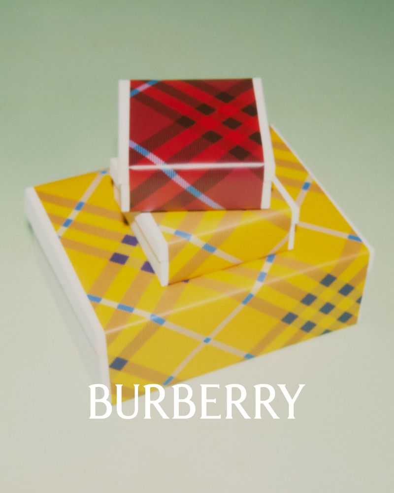 Two Burberry pattern gift boxes, one yellow and one red, stacked on a light green surface with visible brand logo.