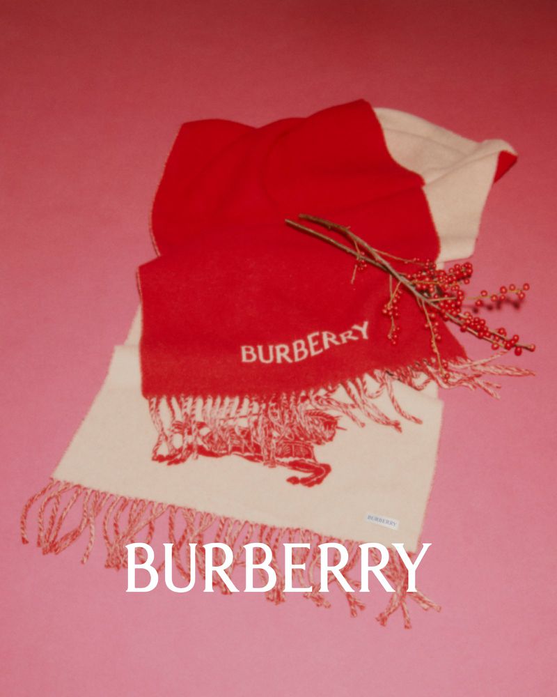 Burberry scarf in red and white with logo, adorned with a small berry branch, set against a pink backdrop.