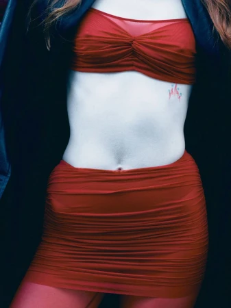 Close-up studio shot of a slim adult female wearing a red bra top and a matching ruched mini skirt in front of a dark background.