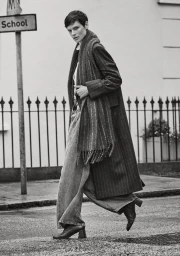 Saskia de Brauw walking in a long pinstripe coat, matching scarf, wide-leg jeans, and heeled boots on a city street.