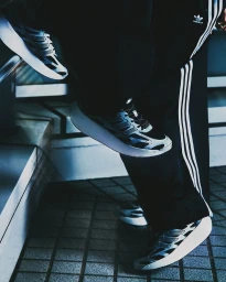 Close-up of Adidas Adizero Aruku sneakers and track pants worn by a model walking down stairs.
