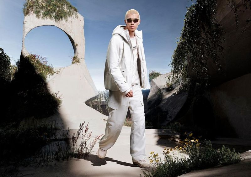 Fashion shot of a person in white hooded jacket and cargo pants in a concrete-sculpture park on a sunny day, showcasing modern apparel.